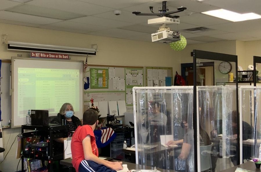 Angela Zlatic reads a novel with her students while they sit separated by clear shower curtains. 
