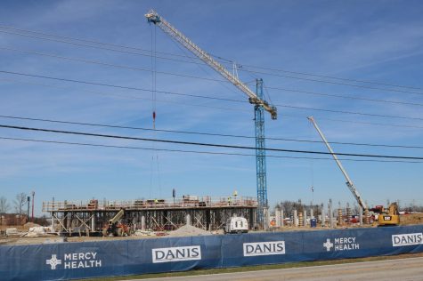 The crane lifts the heavy items back and forth at the construction site across the street from the high school.